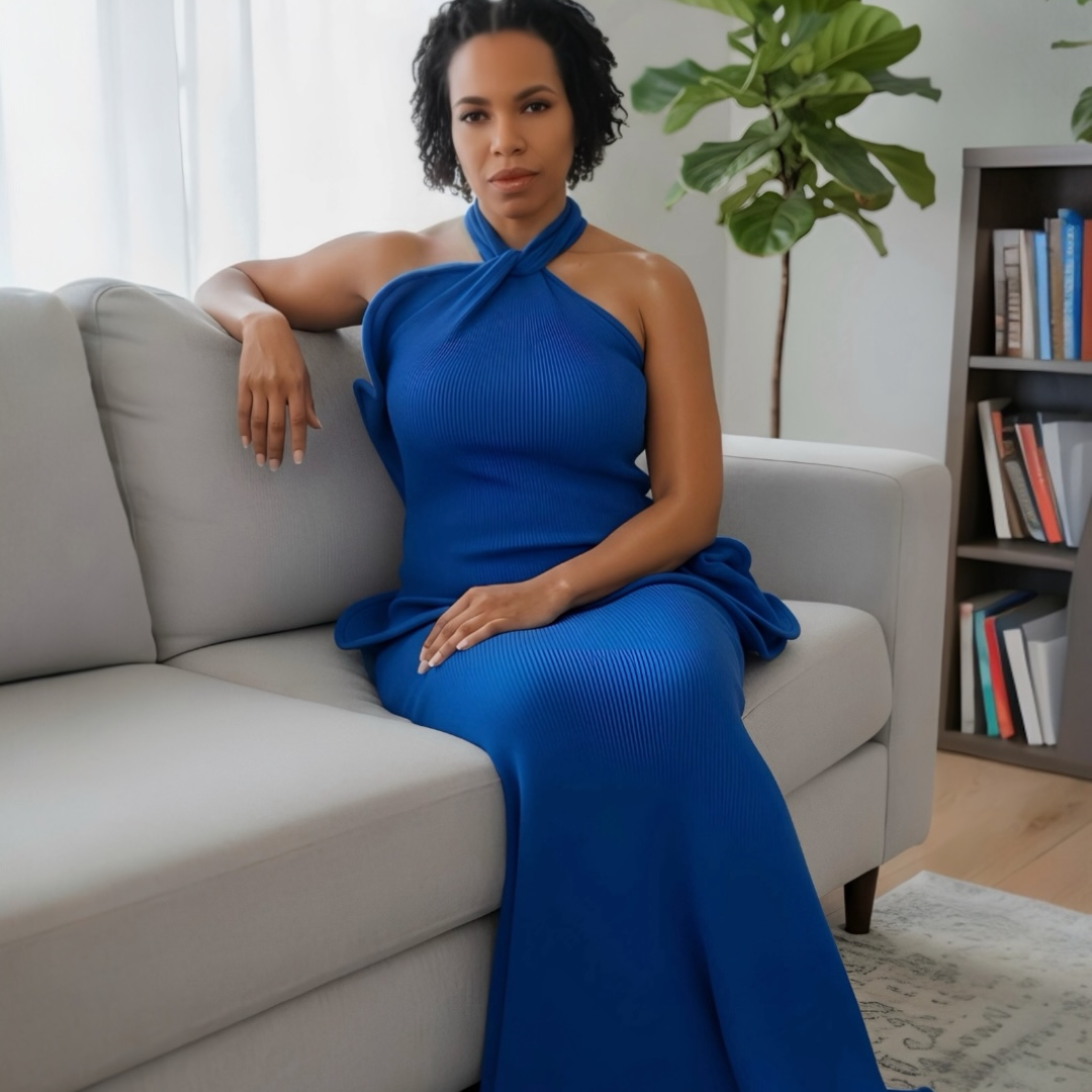 Woman in a blue dress sitting on a gray couch in a living room.